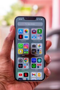 Close-up of hand holding a smartphone with various app icons on the screen outdoors.